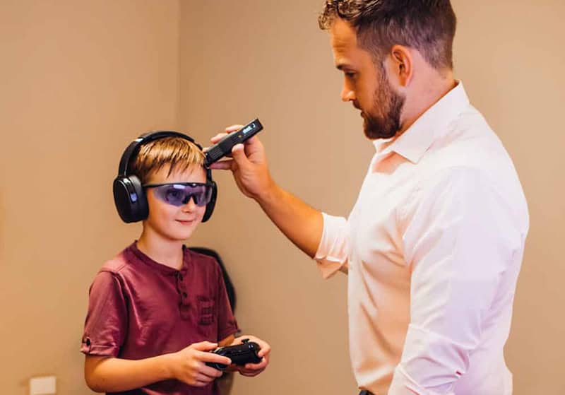 Dr. Sam using cold laser on child while the boy is playing videogame and wearing headphones.
